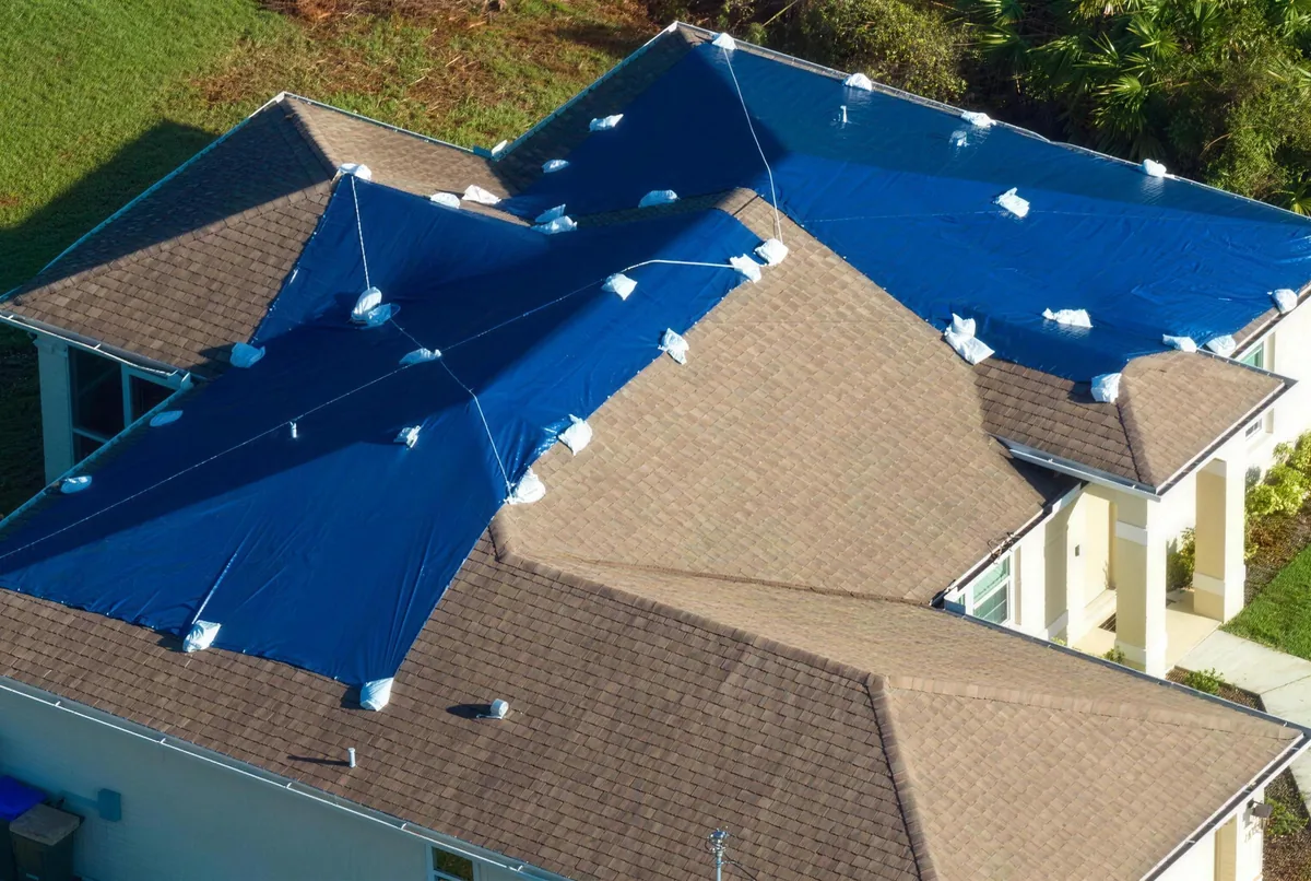 Emergency tarp strapped over a damaged roof section at night