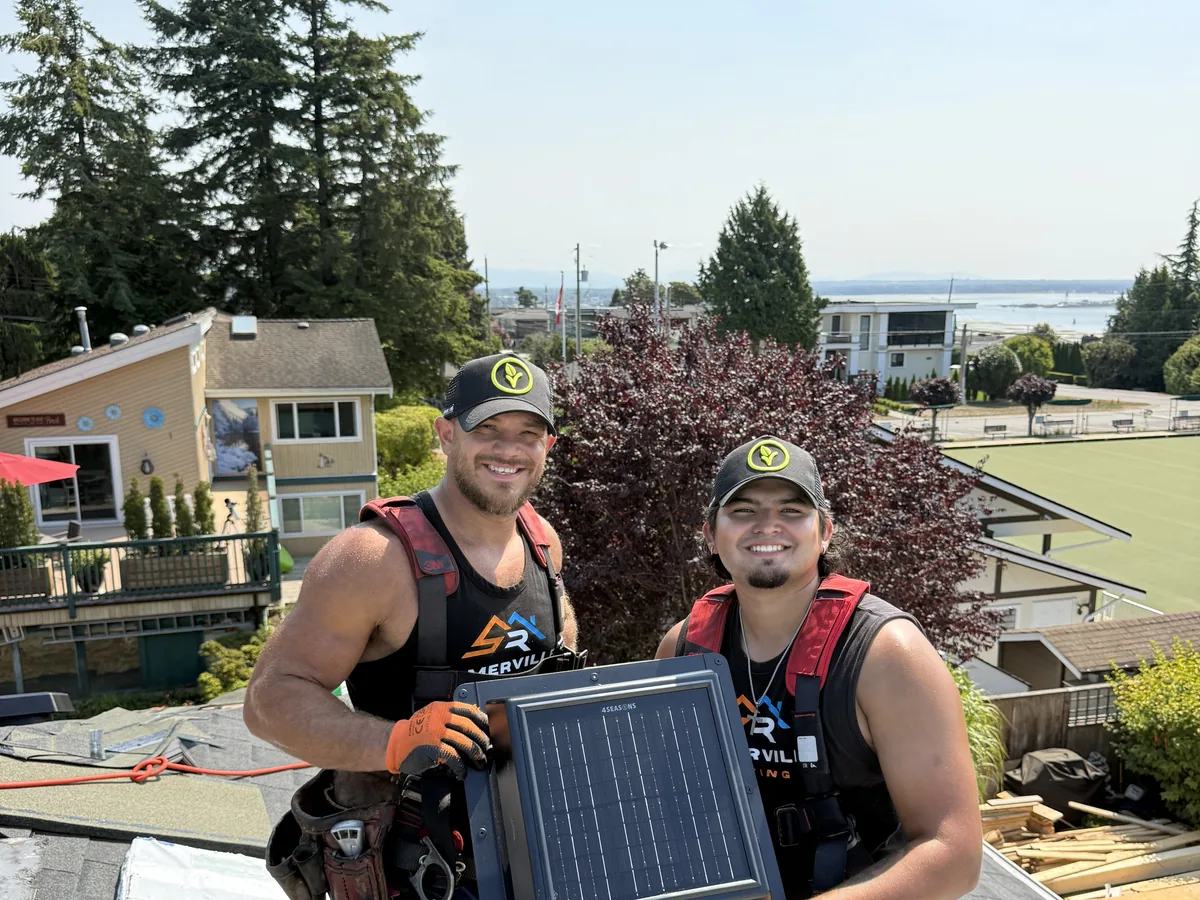 Two Somerville Roofing crew members on a roof holding a 4Seasons solar air vent, with Malarkey Vista AR bundles behind them
